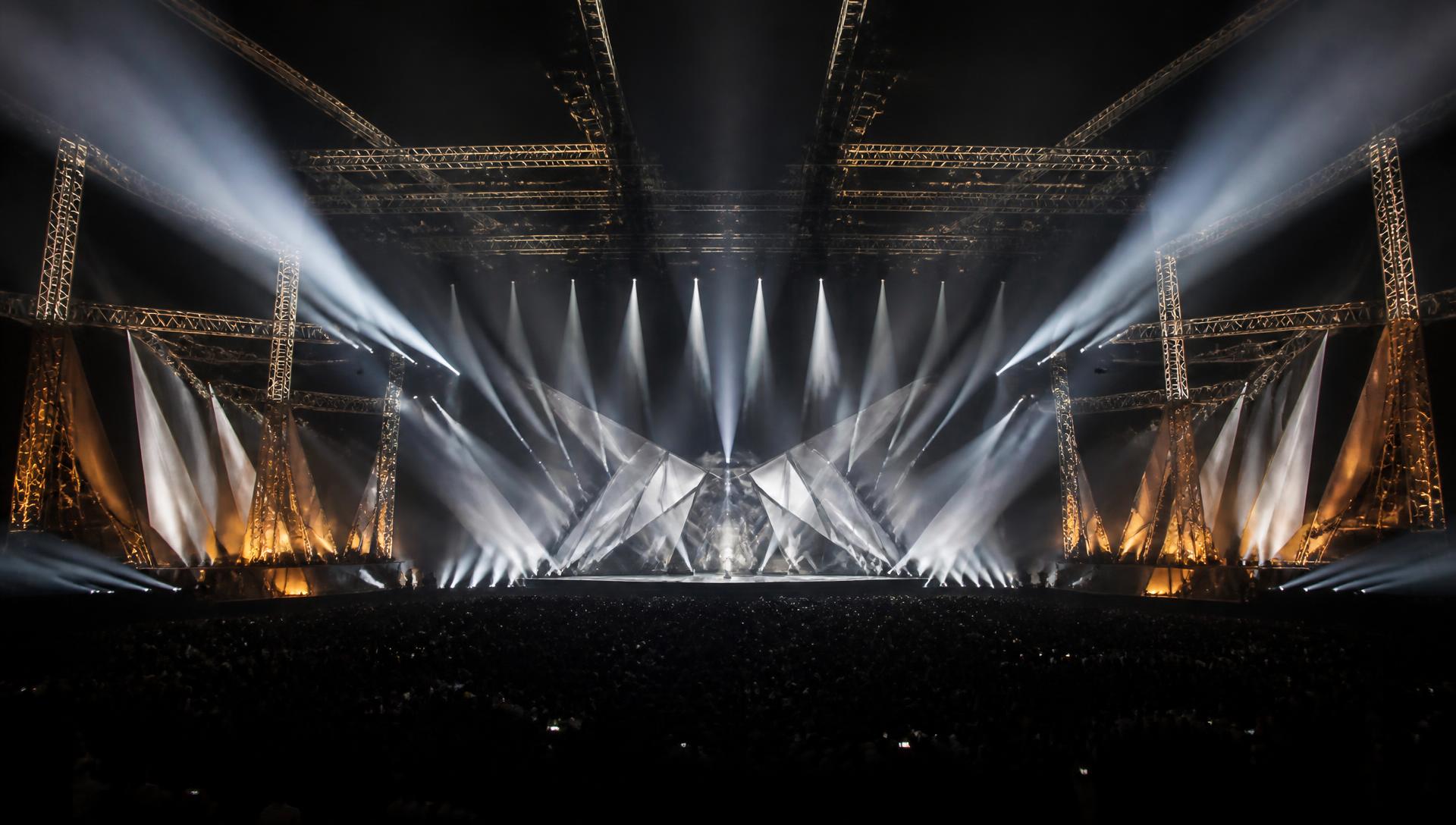 Large-scale concert stage with truss structures and beam lighting over a crowd